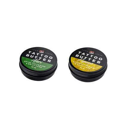 Two tins of Love Ink Tattoo Butter on a transparent background. One tin is labeled 'Tattoo Butter Aloes' with an green design, and the other is labeled 'Tattoo Butter Papaya' with a yellow design. Both tins are 50 ml and are intended for after tattooing and daily care.