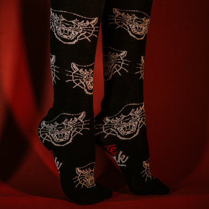 Feet wearing black LOVEINK socks with a white panther head design, posed against a red background.