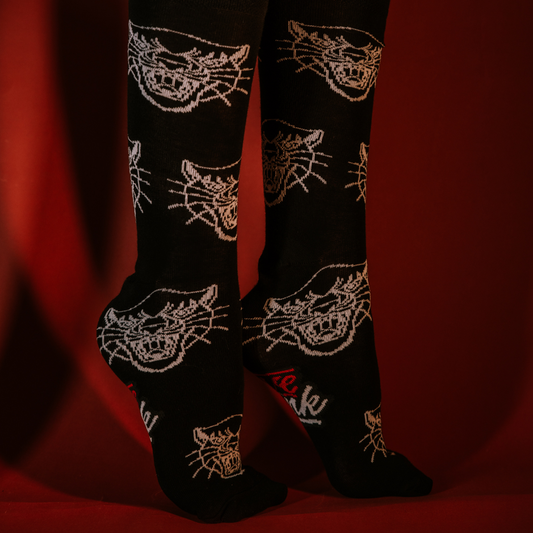 Feet wearing black LOVEINK socks with a white panther head design, posed against a red background.