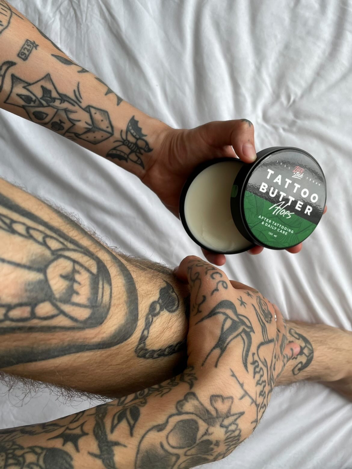 Tattooed person applying Love Ink Tattoo Butter Aloe to their arm, with various tattoos visible.