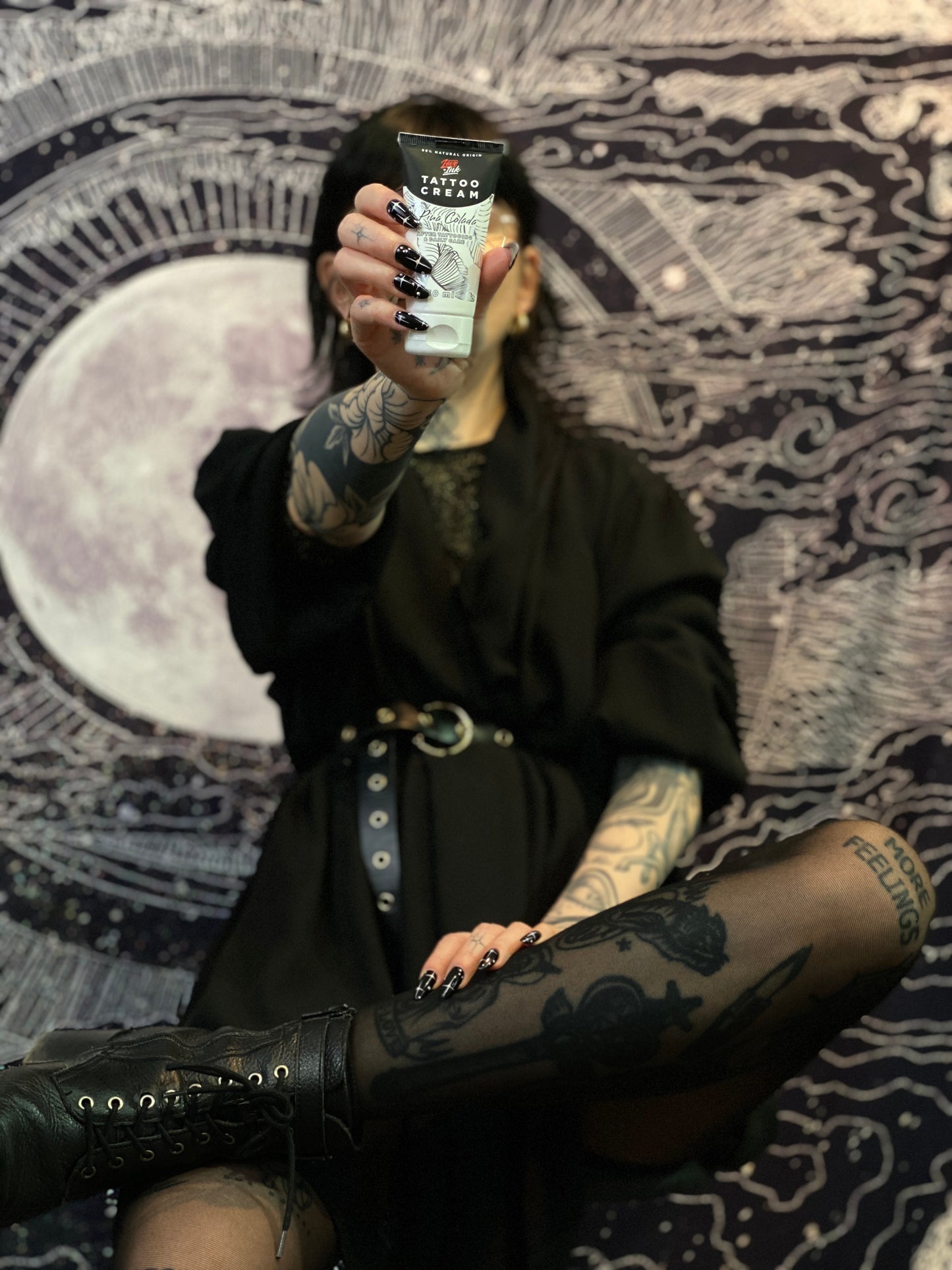 Person holding a tube of Tattoo Cream by LoveInk in front of a detailed, cosmic-themed background, highlighting the product.